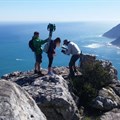 Behind the scenes: #TrekSouthAfrica project lead Andre Van Kets helps Devon Krantz load-up the 22kg Google Trekker backpack as Carte Blanche cameraman Greg Nelson captures the moment with Hout Bay in the background, June 2016. - Photo: Liz Fish