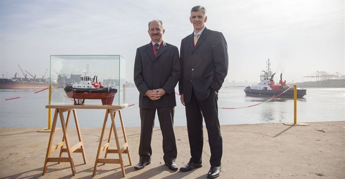 Louis Gontier, Chief Operations Officer of Southern African Shipyards (Left) and Nico Walters, General Manager: Strategy of Transnet National Ports Authority (right) during the official handover of the Port of Durban’s new Umbilo tug from the ship builder to the authority. They are pictured alongside a model of the tug, with the fully built vessel in the background.