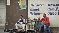 A Tanzanian shoe-shiner conducts his business underneath an election poster for then ruling party presidential candidate, and later president, John Magufuli, in Dar es Salaam, Tanzania, on October 27, 2015. On March 28, 2019, the East African Court of Justice found that multiple sections of Tanzania's Media Services Act restrict press freedom. Credit: CPJ/AP Photo/Khalfan Said.