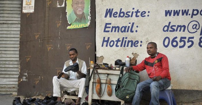 A Tanzanian shoe-shiner conducts his business underneath an election poster for then ruling party presidential candidate, and later president, John Magufuli, in Dar es Salaam, Tanzania, on October 27, 2015. On March 28, 2019, the East African Court of Justice found that multiple sections of Tanzania's Media Services Act restrict press freedom. Credit: CPJ/AP Photo/Khalfan Said.