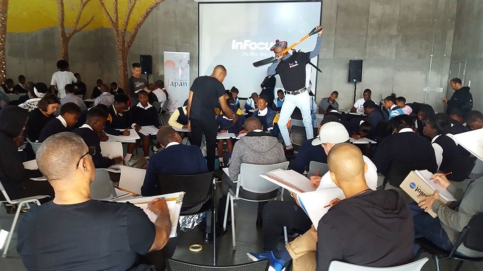 Silhe Mpoyiya poses for an action drawing while joins in the drawing workshop: Sihle Mpoyiya strikes an action pose for the scholars participating in the iKhasi sketchbook workshop. Front left is Oscar winning director Peter Ramsey joining in with the drawing session.