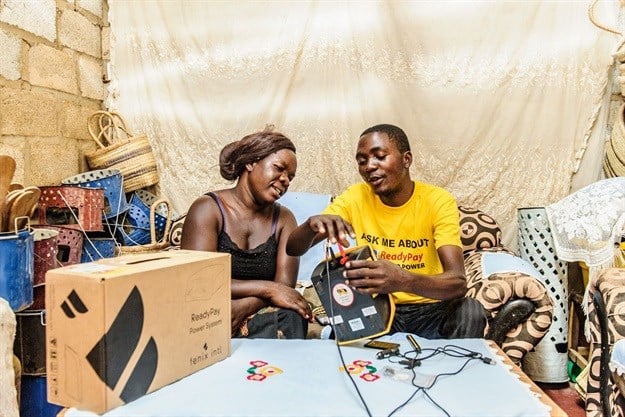 Brian Chitundu (right) works full-time as an agent for Fenix Intl., selling the company’s flagship ReadyPay solar home systems. Here he shows the HomeStarter solar kit to Joyex Zulu (left), a shop owner in Shikoswe Compound, Kafue. Image credit: Jason Mulikita, REEEP