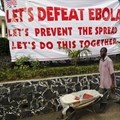 A man pushes a wheelbarrow past a sign in Liberia during the West African Ebola outbreak. AHMED JALLANZO/EPA