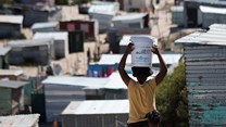 A woman carries a bucket of fresh water to an informal settlement in Khayelitsha, near Cape Town. South Africa has the widest wealth gap in the world. Photo by RODGER BOSCH/AFP via Getty Images