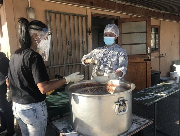 Farida Ryklief dishes out soup to Tasmeen Baatjies for distribution to people in Delft, Cape Town. Photo: Tariro Washinyira