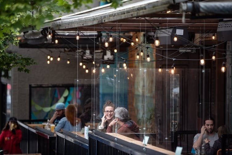 Patrons sit between plexiglass barriers on the patio of a restaurant and bar in Vancouver on May 31, 2020. THE CANADIAN PRESS/Darryl Dyck