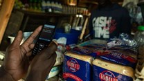 A man makes a payment from his mobile phone for basic food items including bread at a local tuck shop in Epworth, on the outskirts of Harare. Photo by Jekesai Njikizana/AFP via Getty Images
