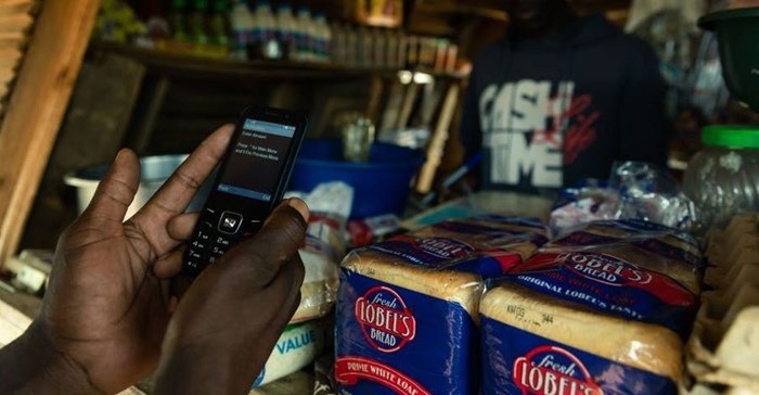 A man makes a payment from his mobile phone for basic food items including bread at a local tuck shop in Epworth, on the outskirts of Harare. Photo by Jekesai Njikizana/AFP via Getty Images