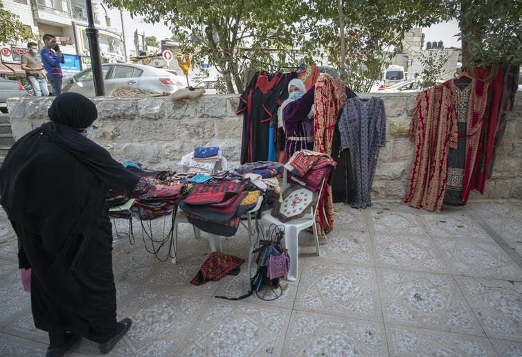 A woman displays a traditional Palestinian embroidery dress to a customer at the Soq al-Fallahat, which means ‘women farmer bazaar,’ in the West Bank city of Ramallah in October 2020. The NGO project, Access Market, targets women handcrafts small enterprises. (AP Photo/Nasser Nasser)