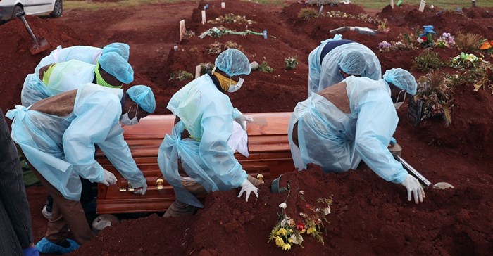 Funeral workers wearing personal protective equipment carry a casket during the burial of a Covid-19 victim, amid a nationwide coronavirus disease (Covid-19) lockdown, at the Olifantsvlei cemetery, south-west of Joburg, South Africa 6 January, 2021. Reuters/Siphiwe Sibeko