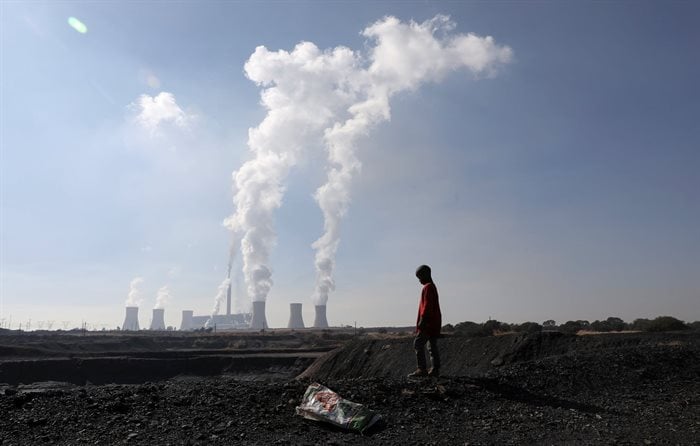A child collecting chunks of coal looks on at a colliery while smoke rises from the Duvha coal-based power station owned by Eskom, in Emalahleni, in Mpumalanga province. Reuters/Siphiwe Sibeko