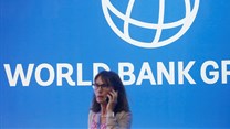 Source: Reuters. A participant stands near a logo of World Bank at the International Monetary Fund - World Bank Annual Meeting 2018 in Indonesia in 2018.