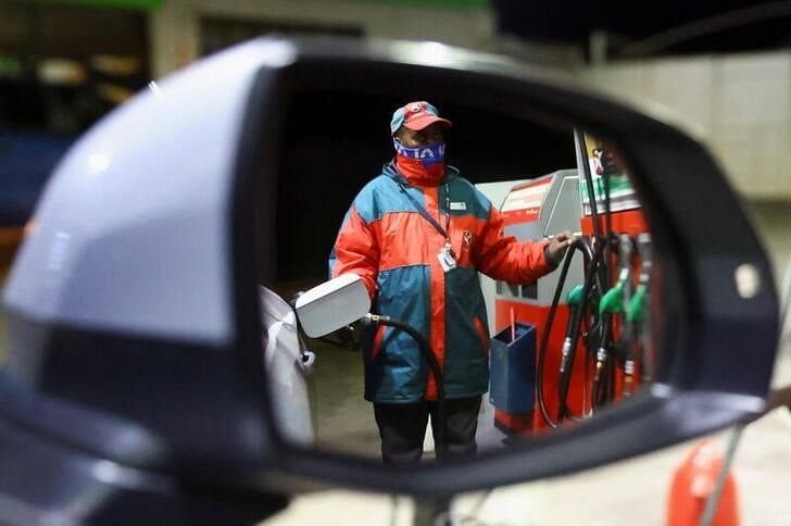 A petrol station attendant is reflected in a side view mirror as he fills up a car ahead of a petrol price increase effective from midnight, at a filling station in Johannesburg on 31 May 2022. Reuters/Siphiwe Sibeko