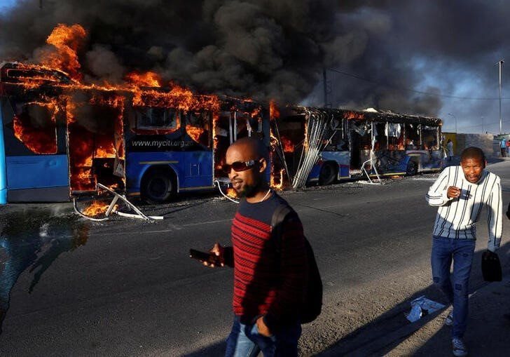 People walk past a torched bus during a two-day strike by taxi operators over a number of grievances against traffic authorities in Cape Town, South Africa, November 21, 2022. REUTERS/Esa Alexander