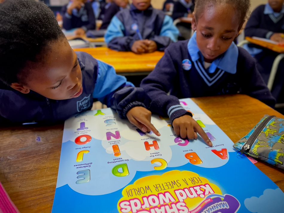 Kefilwe Matlhakoana (left) and Asinalo Tshenge (right) from Asteri Primary School in Gauteng go over the Manhattan Kindness Alphabet poster, a toolkit provided to the school with ideas on ways to be kind.