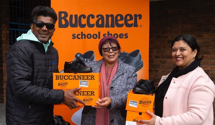 Celebrity performer Loukmaan Adams (left) and Buccaneer School Shoes' Zubeida Abrahams (right) hand over school shoes to Eastville Primary School principal Mrs Heynes