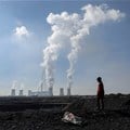 A child collecting chunks of coal looks on at a colliery while smoke rises from the Duvha coal-based power station owned by state power utility Eskom, in Emalahleni. SOurce: Reuters/Siphiwe Sibeko