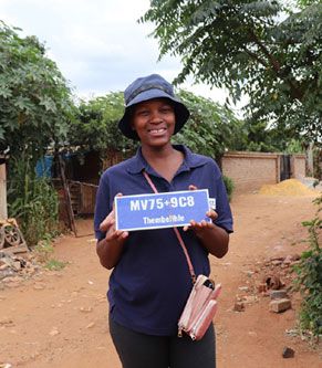 SEF PlanAct - Lerato Qwabe holding a Plus Code address board in Thembelihle.